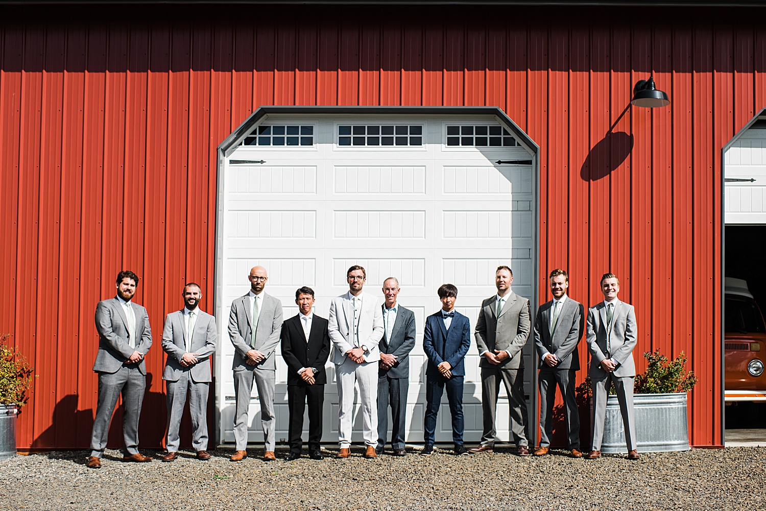 groom's party are standing in front of a red barn while looking straight into the camera