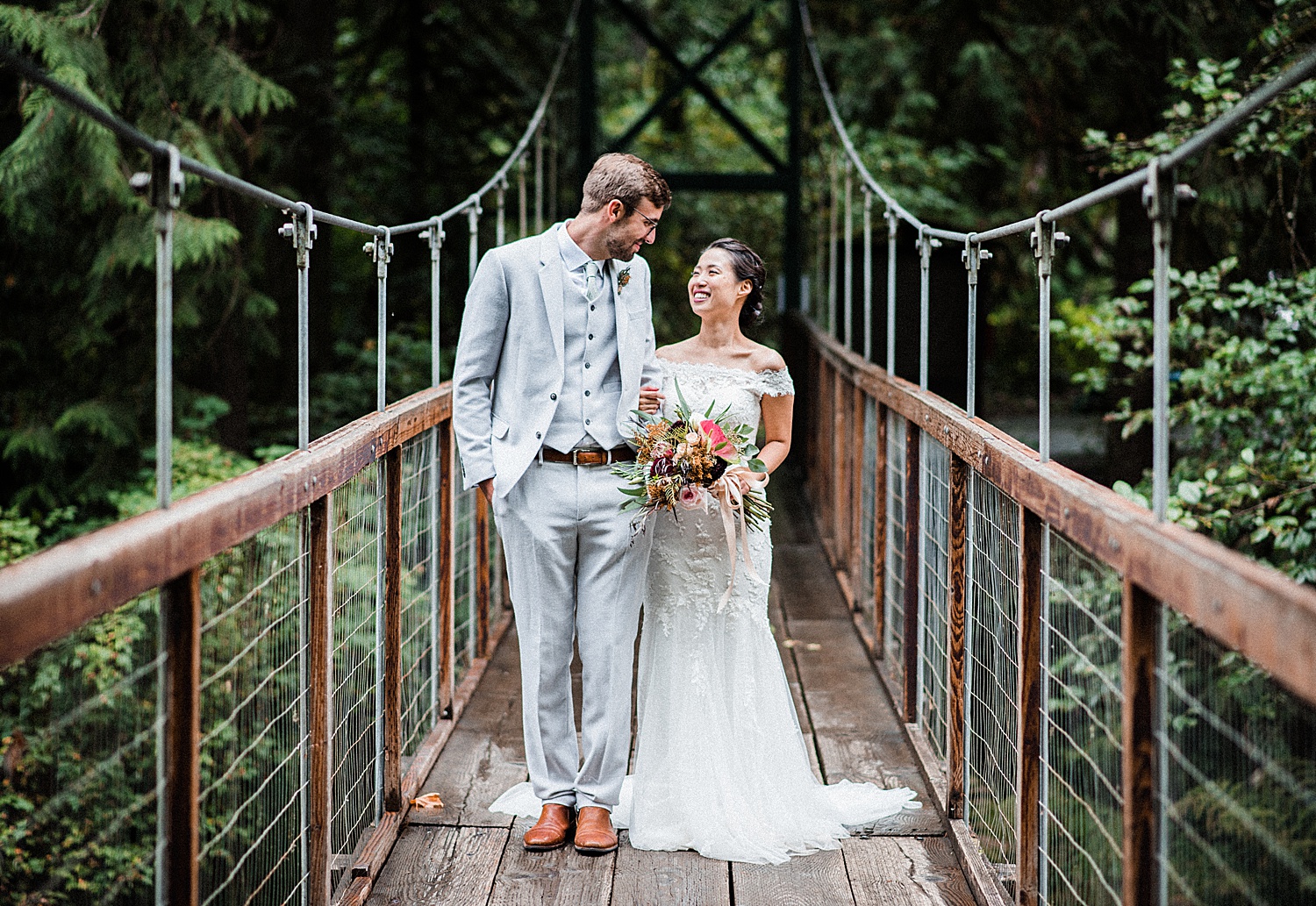 a bride and a groom are smiling at each other standing on a bridge